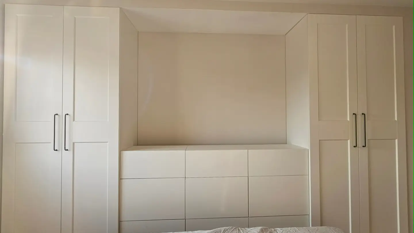 Armario empotrado blanco con cajonera central y puertas laterales en un dormitorio.