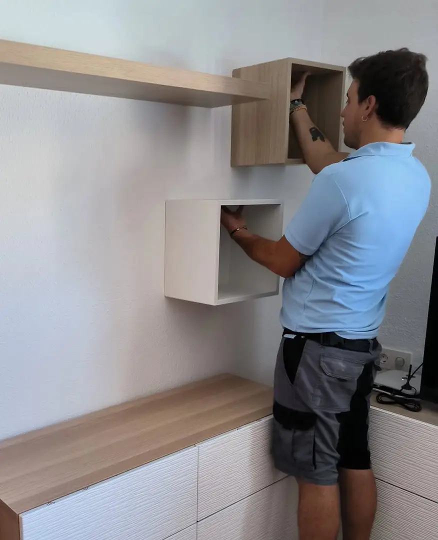 Hombre instalando módulos de madera en la pared como parte de un montaje de muebles en vivienda.